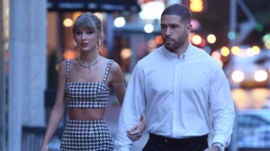“Taylor Swift and Travis Kelce walking together in NYC at dusk, Taylor in a houndstooth Balmain mini dress and Cartier Panthère de Cartier necklace.”