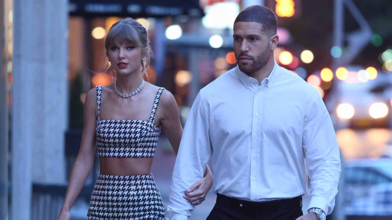 “Taylor Swift and Travis Kelce walking together in NYC at dusk, Taylor in a houndstooth Balmain mini dress and Cartier Panthère de Cartier necklace.”